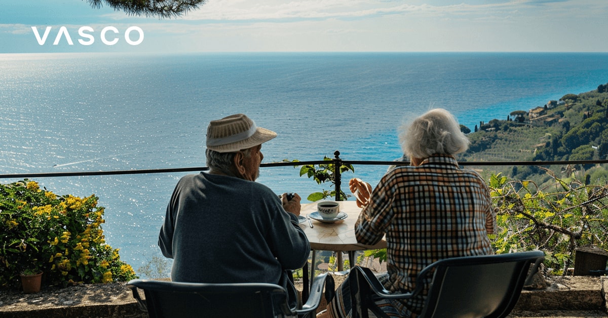 Een ouder echtpaar drinkt koffie op het balkon met uitzicht op zee.