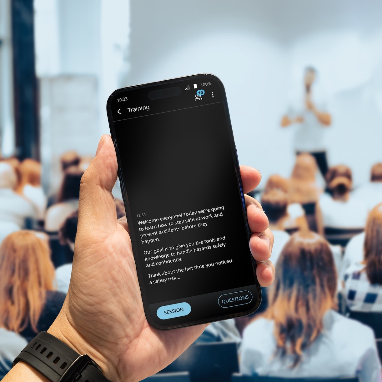 In een zaal vol mensen wordt een lezing gehouden. Een man houdt een telefoon vast waarop de vertaling wordt weergegeven met behulp van Vasco Audience