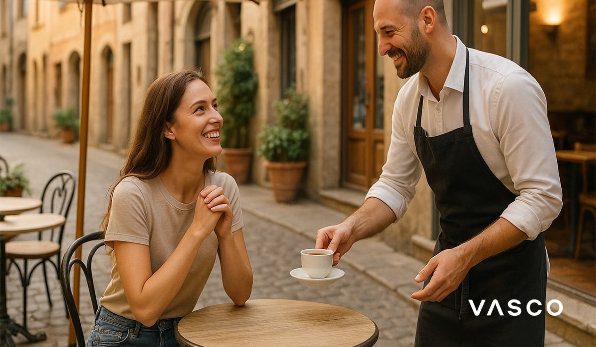 Een ober serveert koffie aan een vrouw die aan een tafeltje zit op een terras.