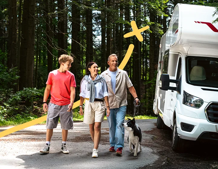 Een gezin van drie – twee ouders en een kind – met een hond, loopt op een zonnige dag weg van hun geparkeerde camper. Ze lachen, praten en genieten van elkaars gezelschap.