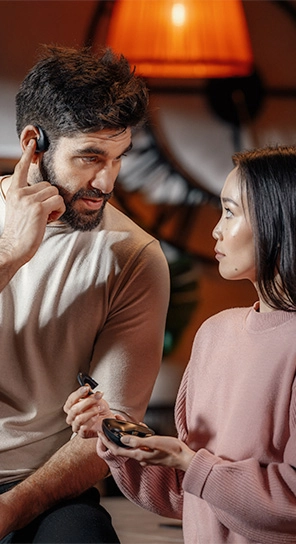 Een man met de Vasco Translator E1-oortje staat naast een vrouw die het E1-apparaat vasthoudt en de krachtige luidsprekers en slimme microfoon demonstreert.