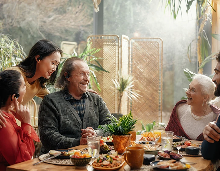 Een gezin zit rond een tafel, met Vasco Translator E1 oortjes in, lachend en pratend met elkaar.