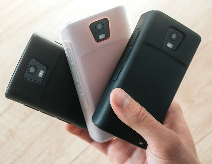 Een persoon met drie Vasco Q1-apparaten in siliconenhoesjes, waarmee drie verschillende kleuren worden getoond: effen zwart, donker karamel en melkwit.